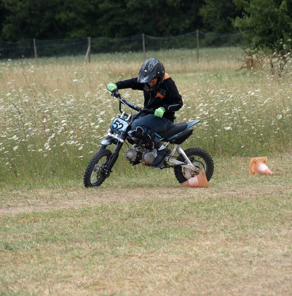 Un enfant sur une moto qui passe entre deux plots dans l'herbe